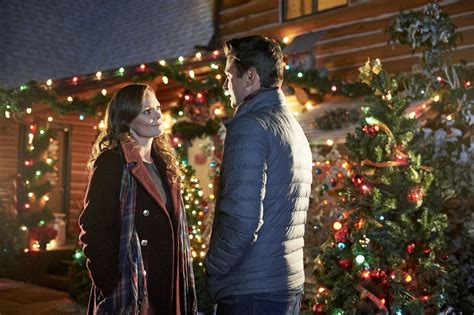 A Man And Woman Standing In Front Of A House With Christmas Lights On