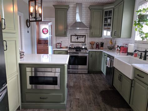 Natural wood cabinets, including dual islands, are topped with white countertops. American Foursquare kitchen. Sage green cabinets, white ...