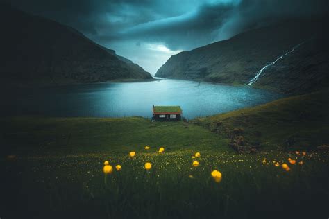 A Small House Sitting On Top Of A Lush Green Hillside Next To A Lake