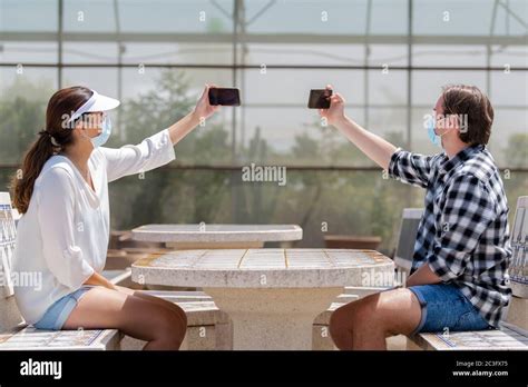 Young Couple Sitting A Table Wearing Surgical Masks Taking Photos Of