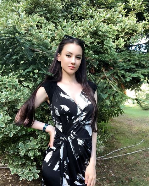 A Woman Standing In Front Of A Bush Wearing A Black Dress With White