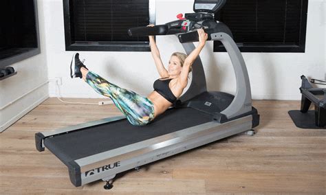 a woman is on a treadmill with her arms in the air and one leg up