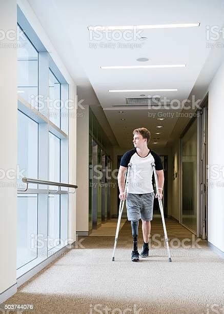 Male Amputee Walking Down Corridor On Crutches Stock Photo Download