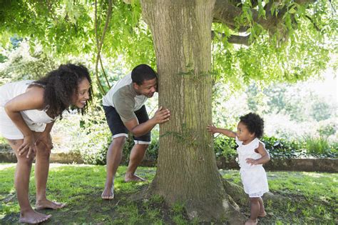 Parents Playing Hide And Seek With Cute Toddler Daughter At Tree Stock