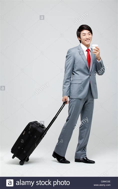 Asian Businessman Walking With Luggage Holding Takeaway Coffee Stock