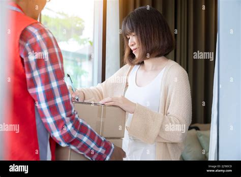 Rear Of Delivery Man In Red Uniform Holding Package While Client Woman