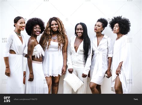A Group Of Black Women Wearing White Attire Pose In Front Of A White