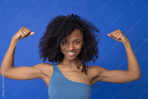 Smiling Woman Flexing Muscles Against Blue Background Stock Photo