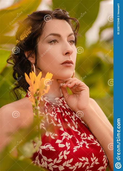 a beautiful girl in a red dress and with earrings in the rings in the greenhouse woman in