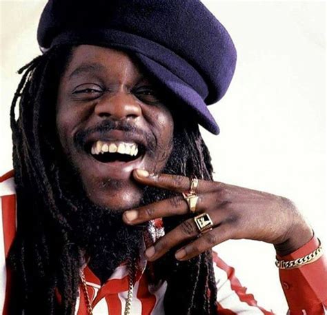 A Man With Dreadlocks Is Smiling And Holding His Finger Up To His Mouth