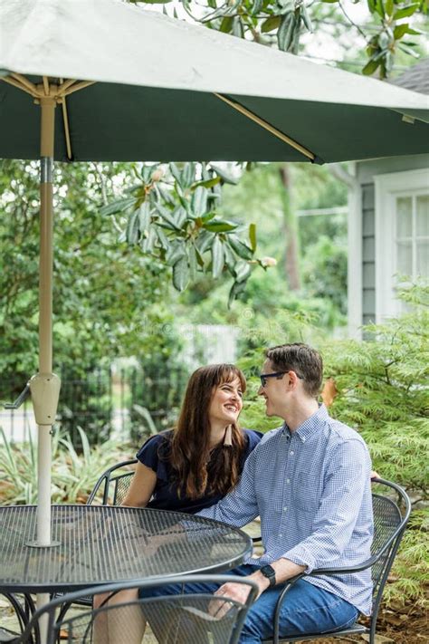 acouple of a husband and wife sitting under a shaded umbrella patio table outside in the