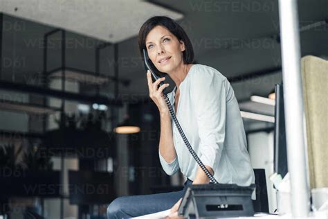 Mature Businesswoman Talking Through Landline Phone In Office Stock Photo