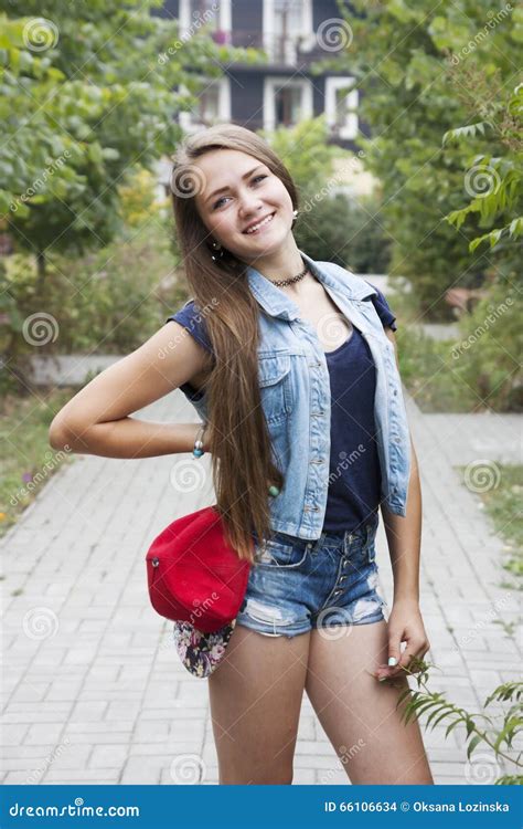 Tween Girl With Trendy Pink Hair Wearing Jeans Smiles Slightly While Bracing Herself On