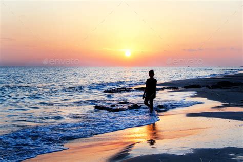 Silhouette Of A Young Woman Walking At The Beach In Front Of The Sunset