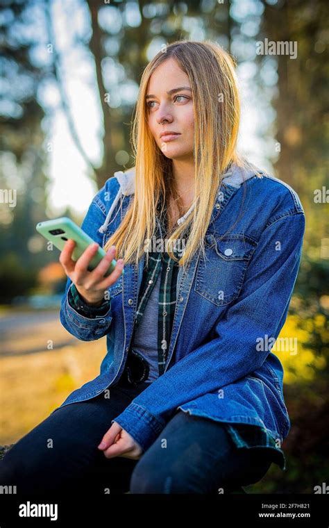 cute blonde girl with long hair septum piercing and jeans shirt using her telephone in a park