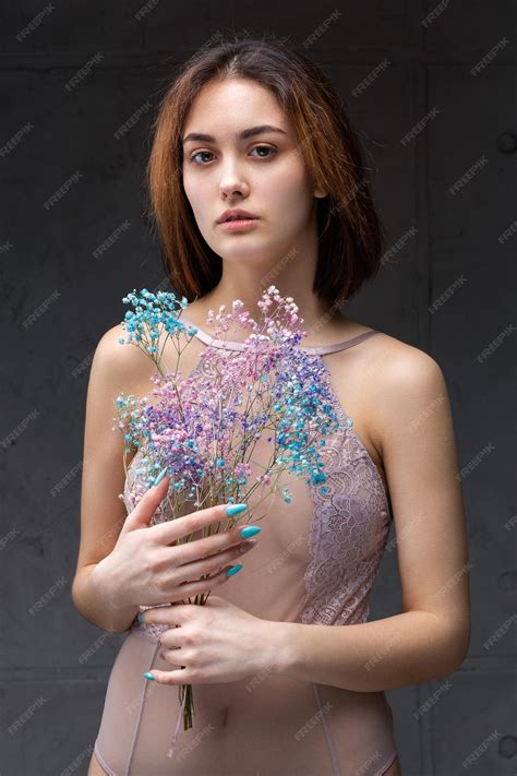 エレガントなヌードのボディースーツを着た美しいセクシーな女性が彼女の手に花を持っていますスタジオでファッションモデルの女の子のファッションの美しさの肖像画 プレミアム写真
