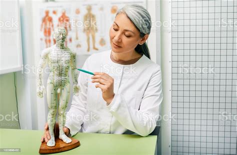 Mature Woman Acupuncturist Doctor Of Traditional Chinese Medicine Showing Points On Acupuncture