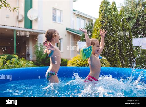 Two Cheerful Cute Little Sisters Playing And Having Fun Splashing And Jumping In Inflatable