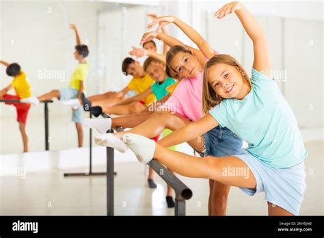 Happy Preteen Girl Warming Up Near Ballet Bar During Group Class Stock