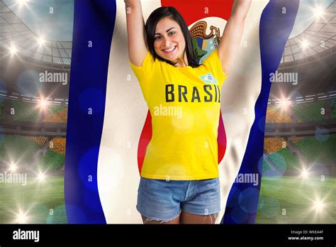 Excited Football Fan In Brasil Tshirt Holding Costa Rica Flag Against Large Football Stadium