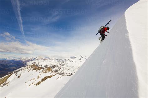 Man With Skis On Back Climbing Snowy Mountain Stock Photo