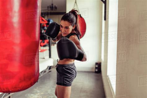 Fit Young Woman Boxer Punching A Bag In The Gym As She Works Out With A