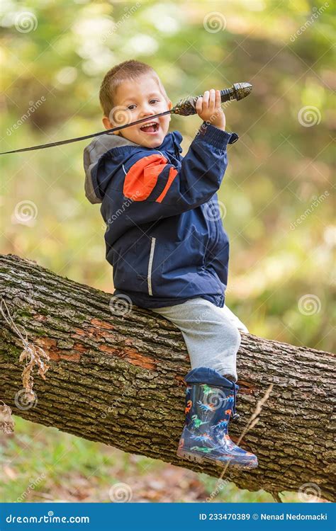 Kleiner Junge Sitzt Auf Gefallenem Baumstamm Und Spielt Mit Einem Schwert Stockbild Bild Von