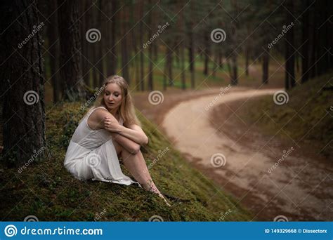 Beautiful Young Blonde Woman Sitting In Forest Nymph In White Dress In