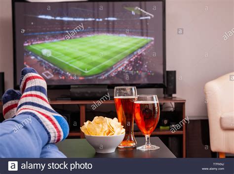Relaxed Man Lying On Sofa While Watching Football Match On Television