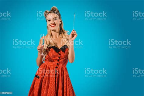 pretty pin up woman in vintage clothing with sparkler and glass of champagne on blue backdrop
