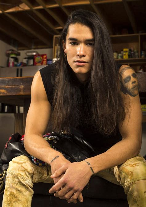 A Man With Long Hair And Tattoos Sitting On A Couch In Front Of A Table