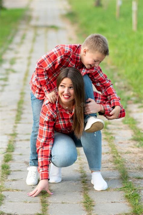 Mom With A Surprised Expression On Her Face Squatting Down Holds A Laughing Son On His