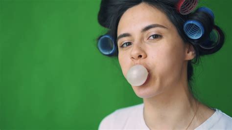 girl with curlers on her head and chewing gum blowing bubbles on a green background chromakey