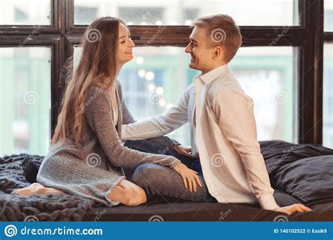 Young Man And Woman In Bed Are Sitting Opposite Each Other Stock Photo