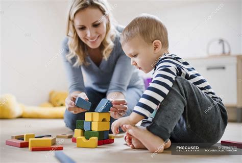 Smiling Mother And Toddler Son Playing With Building Blocks At Home