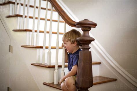 Boy Crying While Sitting On Staircase At Home Stock Photo