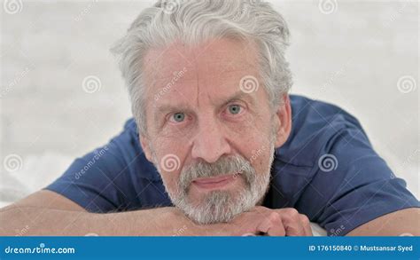Close Up Of Senior Old Man Lying In Bed And Looking At Camera Stock