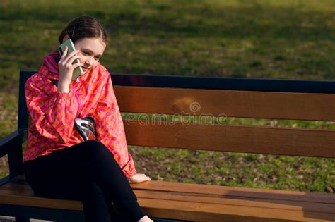 Child Girl Sitting On A Bench And Smiling While Talking On The Phone