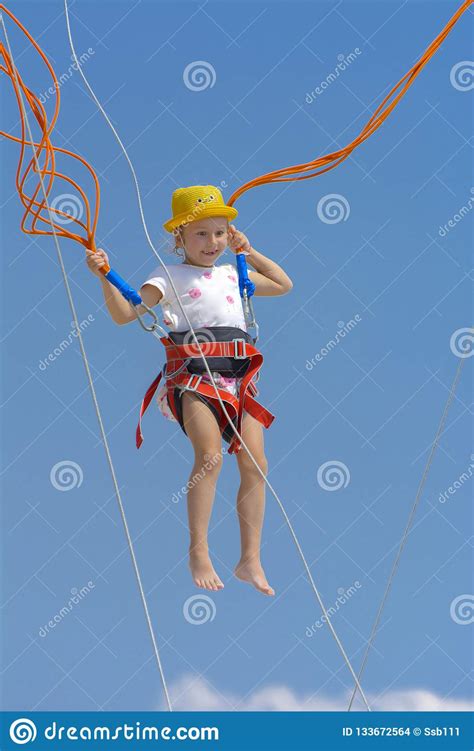 Jump high on the trampoline, bring the legs up with the toes pointed forward and reach forward to touch your toes. A Little Girl Jumps High On A Trampoline With Rubber Ropes ...