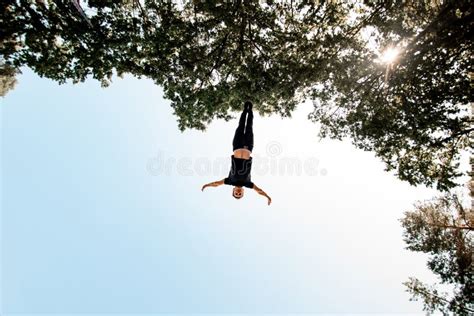 View Of Man Jumps High In The Air Against Blue Sky And Green Trees