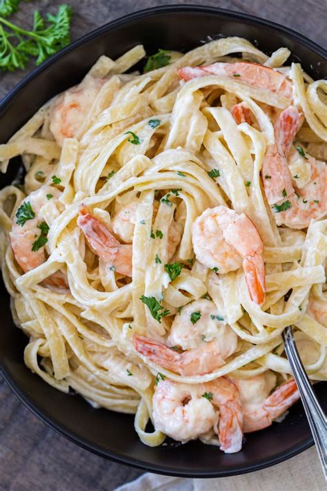 Pasta With Shrimp And Parsley In A Black Bowl On Top Of A Wooden Table