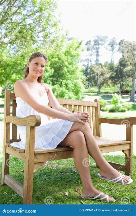 Smiling Woman With Her Legs Crossed Sitting On A Park Bench Stock Photo