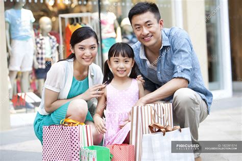 Chinese Parents And Daughter Posing With Shopping Bags In Mall