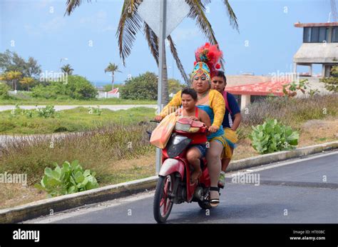A Mexican Woman Rides A Moped Scooter With Her Sons To The Carnival In