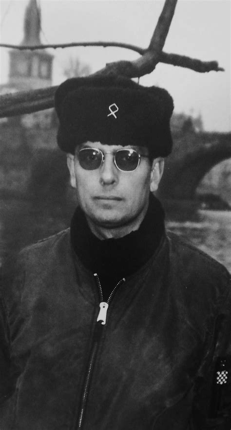 A Man Wearing Sunglasses And A Hat Standing Next To A Tree
