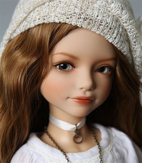 A Close Up Of A Doll Wearing A White Dress And Hat With Pearls On Its Head