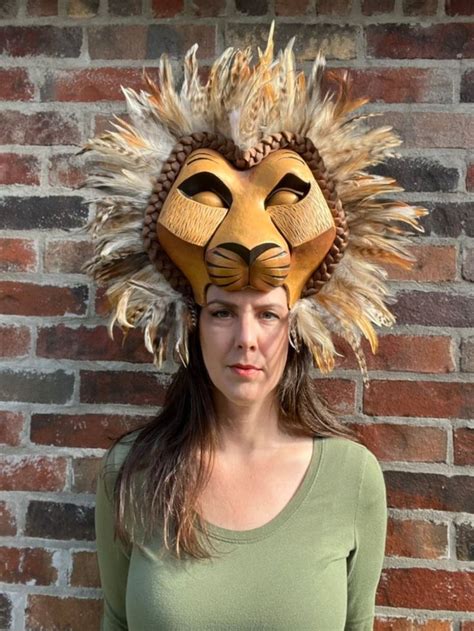A Woman Standing In Front Of A Brick Wall With A Lion Mask On Her Head