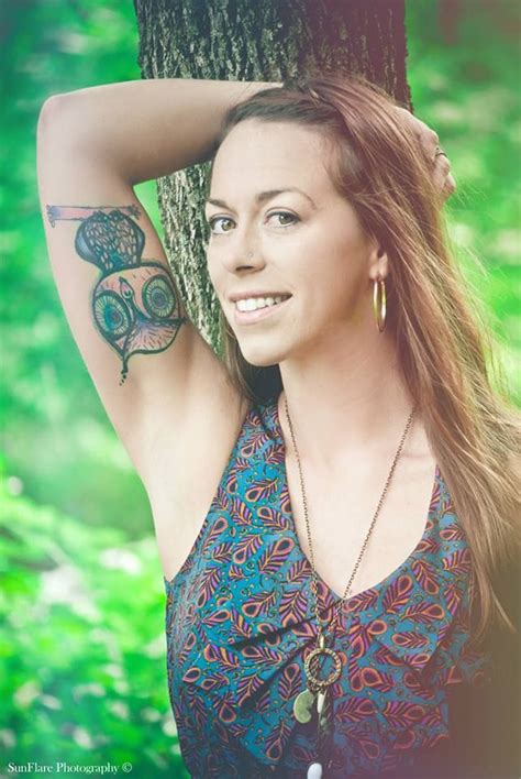 A Woman Standing Next To A Tree With Tattoos On Her Arm