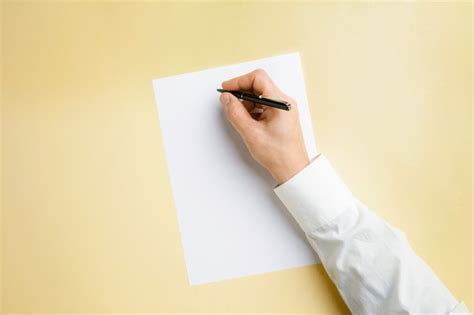 Мужская рука держит ручку и писать на пустой лист на желтой стене для