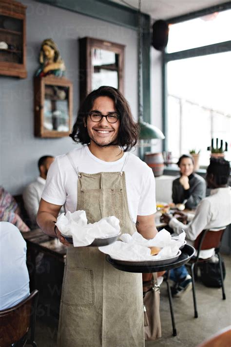 Portrait Of Confident Young Waiter Serving Food While Standing Against